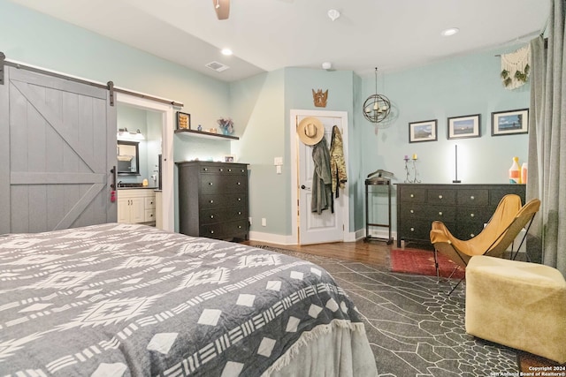 bedroom featuring a barn door, ceiling fan, dark hardwood / wood-style floors, and ensuite bath