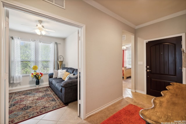 tiled foyer with ceiling fan and crown molding