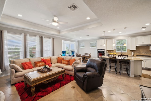 tiled living room with a tray ceiling, ceiling fan, sink, and crown molding