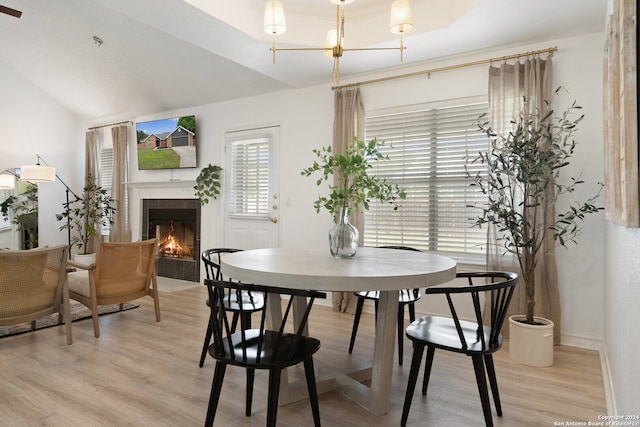 dining area with light wood-type flooring, lofted ceiling, a tiled fireplace, and a notable chandelier