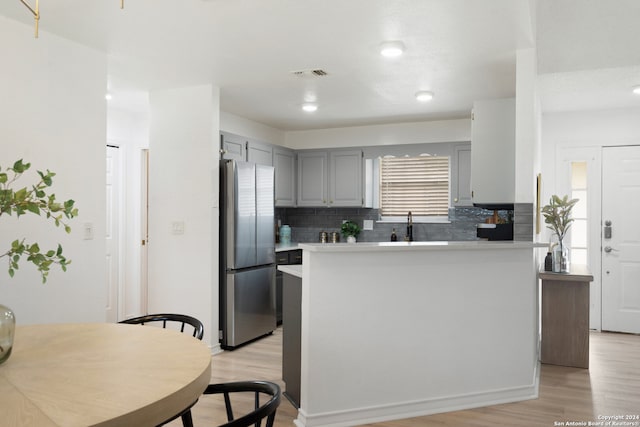 kitchen featuring gray cabinets, a kitchen island, light hardwood / wood-style flooring, decorative backsplash, and stainless steel fridge