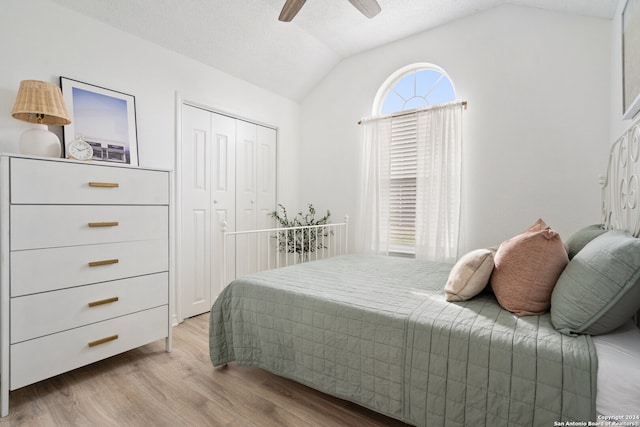 bedroom featuring a closet, light hardwood / wood-style floors, a textured ceiling, vaulted ceiling, and ceiling fan