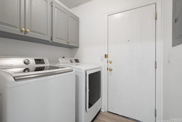 clothes washing area featuring a textured ceiling, light hardwood / wood-style flooring, cabinets, electric panel, and washer and dryer