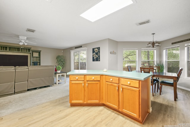 kitchen with ceiling fan with notable chandelier, a center island, a skylight, and plenty of natural light