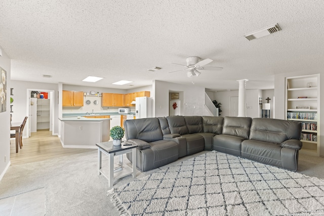 living room with a textured ceiling, decorative columns, light carpet, and ceiling fan