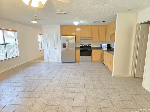 kitchen featuring light tile patterned floors, stainless steel appliances, a textured ceiling, light brown cabinetry, and ceiling fan