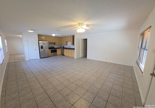 unfurnished living room with ceiling fan, sink, light tile patterned floors, and a textured ceiling