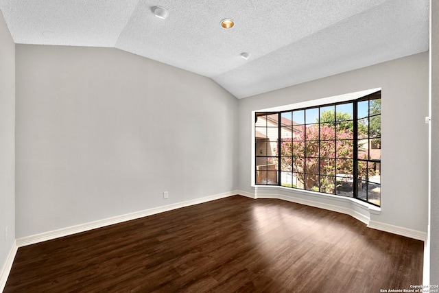 spare room with a textured ceiling, vaulted ceiling, and dark hardwood / wood-style flooring