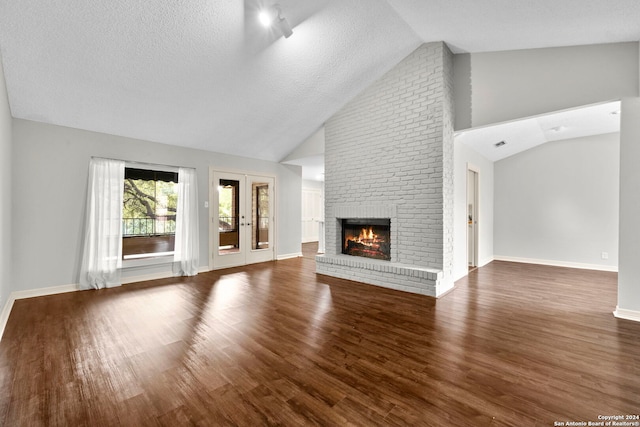 unfurnished living room featuring high vaulted ceiling, a fireplace, dark hardwood / wood-style flooring, a textured ceiling, and french doors