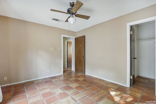 unfurnished bedroom with a closet, a textured ceiling, a walk in closet, tile patterned floors, and ceiling fan