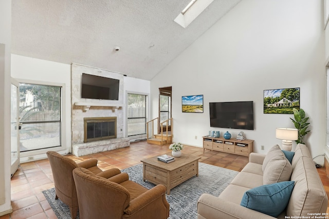 living room featuring a skylight, a textured ceiling, high vaulted ceiling, a fireplace, and tile patterned flooring