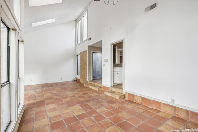 tiled empty room with a towering ceiling and a skylight