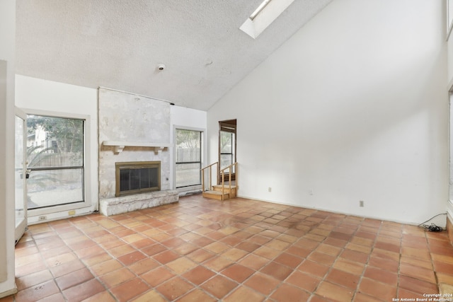 unfurnished living room with a skylight, light tile patterned floors, a textured ceiling, high vaulted ceiling, and a large fireplace