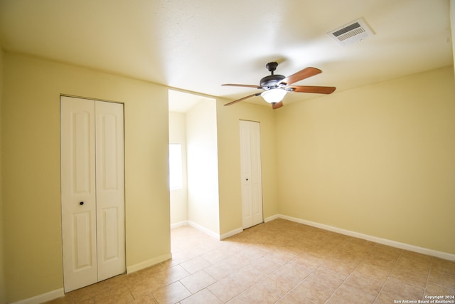 unfurnished bedroom featuring two closets, light tile patterned floors, and ceiling fan