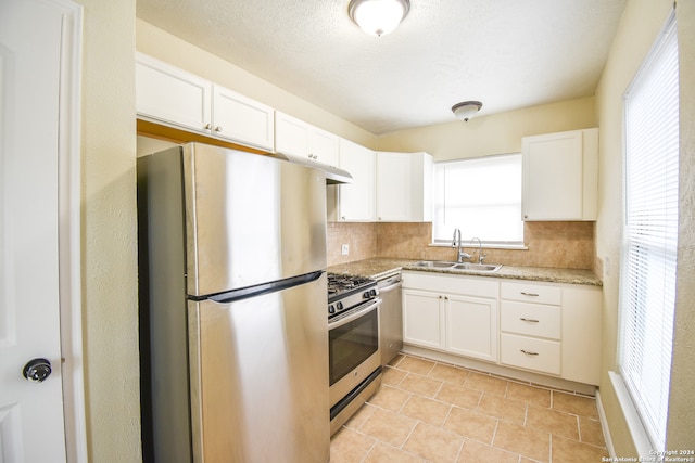 kitchen with appliances with stainless steel finishes, sink, backsplash, white cabinetry, and light stone counters