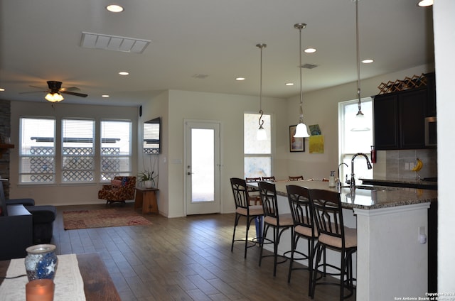 kitchen featuring pendant lighting, a breakfast bar, dark wood-type flooring, dark stone countertops, and ceiling fan