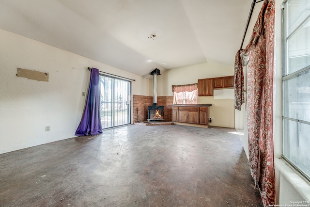 unfurnished living room featuring concrete flooring, lofted ceiling, and a wood stove