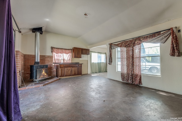 unfurnished living room with concrete flooring, vaulted ceiling, a wealth of natural light, and a wood stove