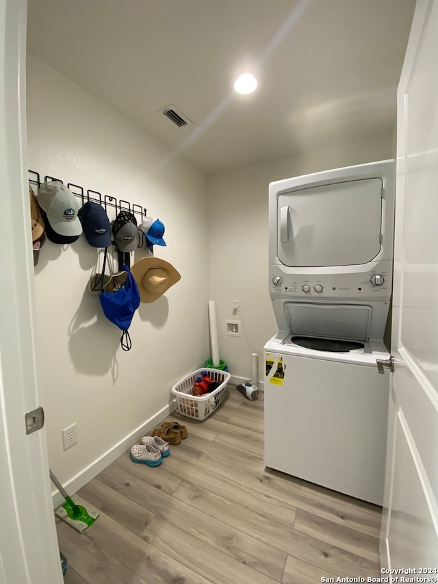 clothes washing area with stacked washing maching and dryer and light hardwood / wood-style flooring