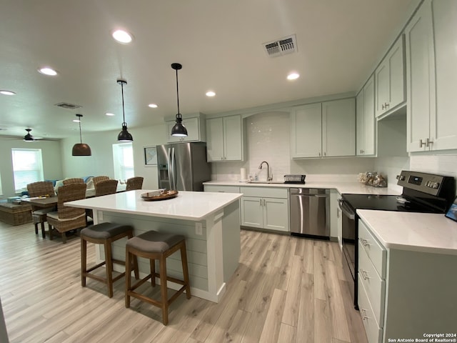 kitchen with appliances with stainless steel finishes, a kitchen island, light wood-type flooring, ceiling fan, and decorative light fixtures