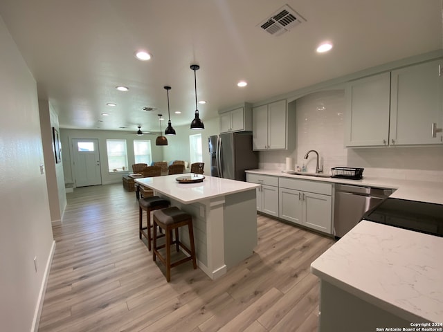 kitchen with pendant lighting, sink, a kitchen island, appliances with stainless steel finishes, and light wood-type flooring