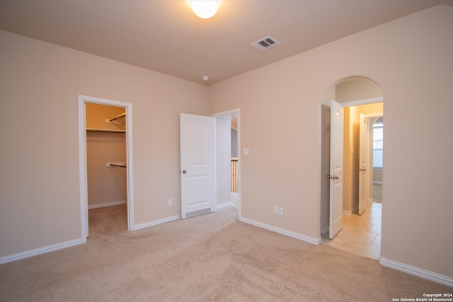 unfurnished bedroom with a spacious closet, light colored carpet, and a closet