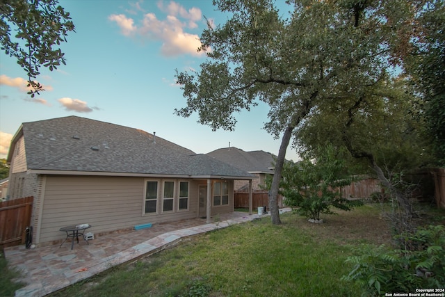 back house at dusk featuring a lawn and a patio area