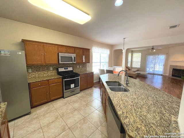 kitchen featuring ceiling fan, light stone counters, sink, stainless steel appliances, and a fireplace