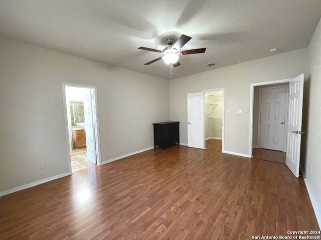 unfurnished bedroom with a spacious closet, ensuite bath, ceiling fan, and dark wood-type flooring