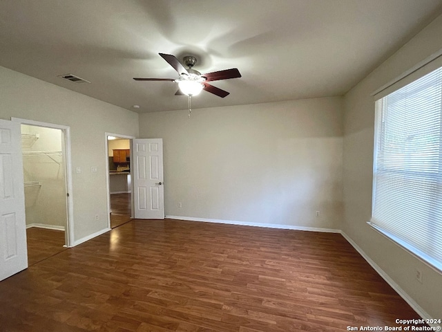 unfurnished bedroom featuring dark hardwood / wood-style floors, ceiling fan, a walk in closet, and a closet