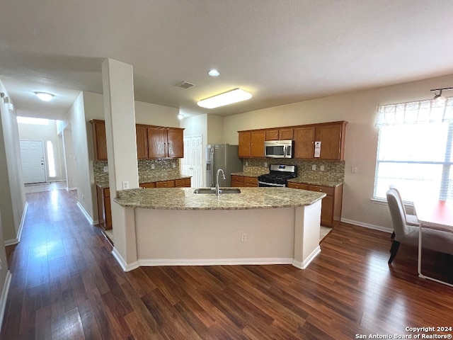 kitchen with appliances with stainless steel finishes, sink, dark wood-type flooring, and light stone counters