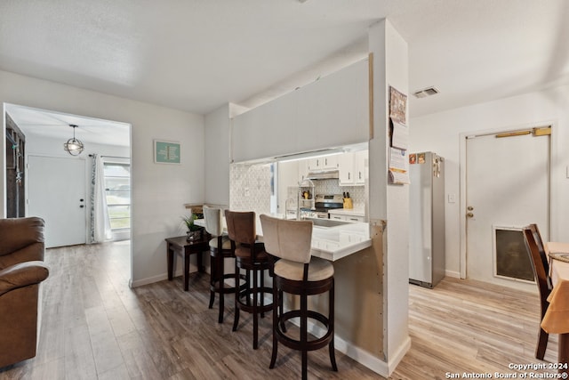 kitchen with white cabinets, kitchen peninsula, stainless steel appliances, light hardwood / wood-style flooring, and decorative light fixtures