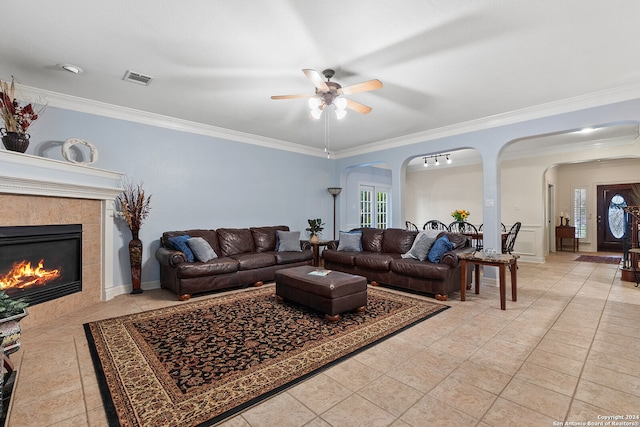 living room featuring a wealth of natural light, ceiling fan, a tile fireplace, and crown molding