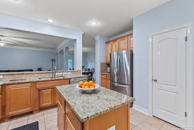 kitchen featuring a center island, sink, appliances with stainless steel finishes, light stone countertops, and ceiling fan