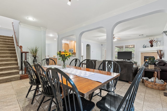 tiled dining area featuring ornamental molding, decorative columns, ceiling fan, and a tile fireplace