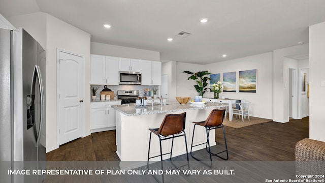 kitchen featuring appliances with stainless steel finishes, light stone counters, white cabinets, dark hardwood / wood-style flooring, and a center island with sink