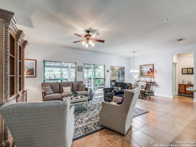 living room with ceiling fan, a textured ceiling, a brick fireplace, and light tile patterned floors