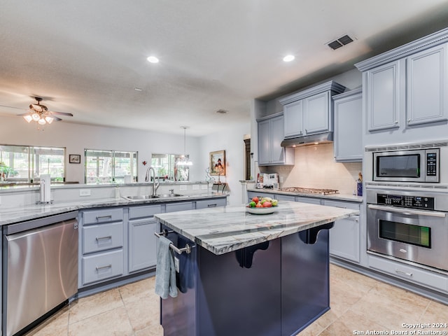 kitchen with appliances with stainless steel finishes, a breakfast bar, light stone countertops, ceiling fan, and sink