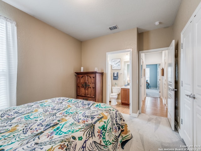 bedroom featuring light colored carpet, a closet, and ensuite bath