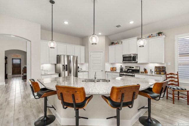 kitchen with appliances with stainless steel finishes, a large island with sink, sink, and white cabinetry