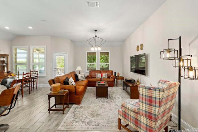 living room with an inviting chandelier, light hardwood / wood-style flooring, plenty of natural light, and lofted ceiling