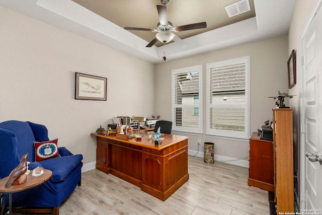 office area with light hardwood / wood-style flooring, a tray ceiling, and ceiling fan