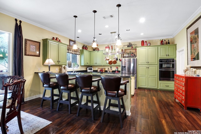 kitchen with a breakfast bar, green cabinetry, appliances with stainless steel finishes, and hanging light fixtures