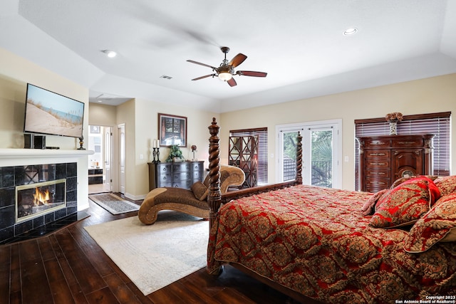 bedroom with ceiling fan, a tiled fireplace, access to exterior, dark hardwood / wood-style floors, and vaulted ceiling