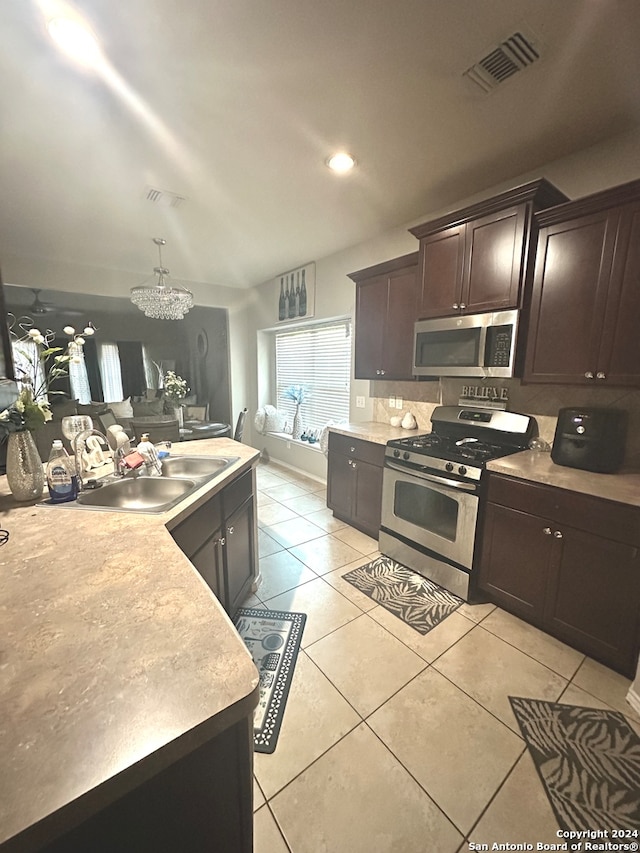 kitchen with dark brown cabinets, stainless steel appliances, sink, an inviting chandelier, and light tile patterned floors