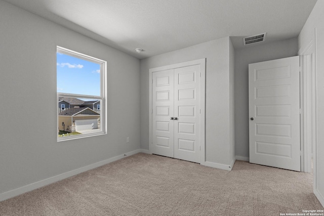 unfurnished bedroom with light colored carpet, a textured ceiling, and a closet