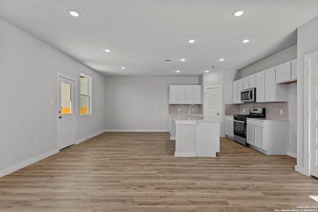 kitchen with appliances with stainless steel finishes, white cabinetry, light hardwood / wood-style flooring, and a kitchen island with sink