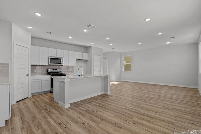 kitchen with white cabinetry, a kitchen island with sink, light hardwood / wood-style floors, and appliances with stainless steel finishes