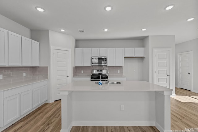 kitchen with white cabinetry, light hardwood / wood-style flooring, a kitchen island with sink, and appliances with stainless steel finishes