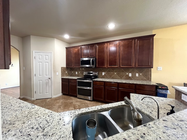 kitchen with light tile patterned floors, sink, stainless steel appliances, light stone countertops, and decorative backsplash